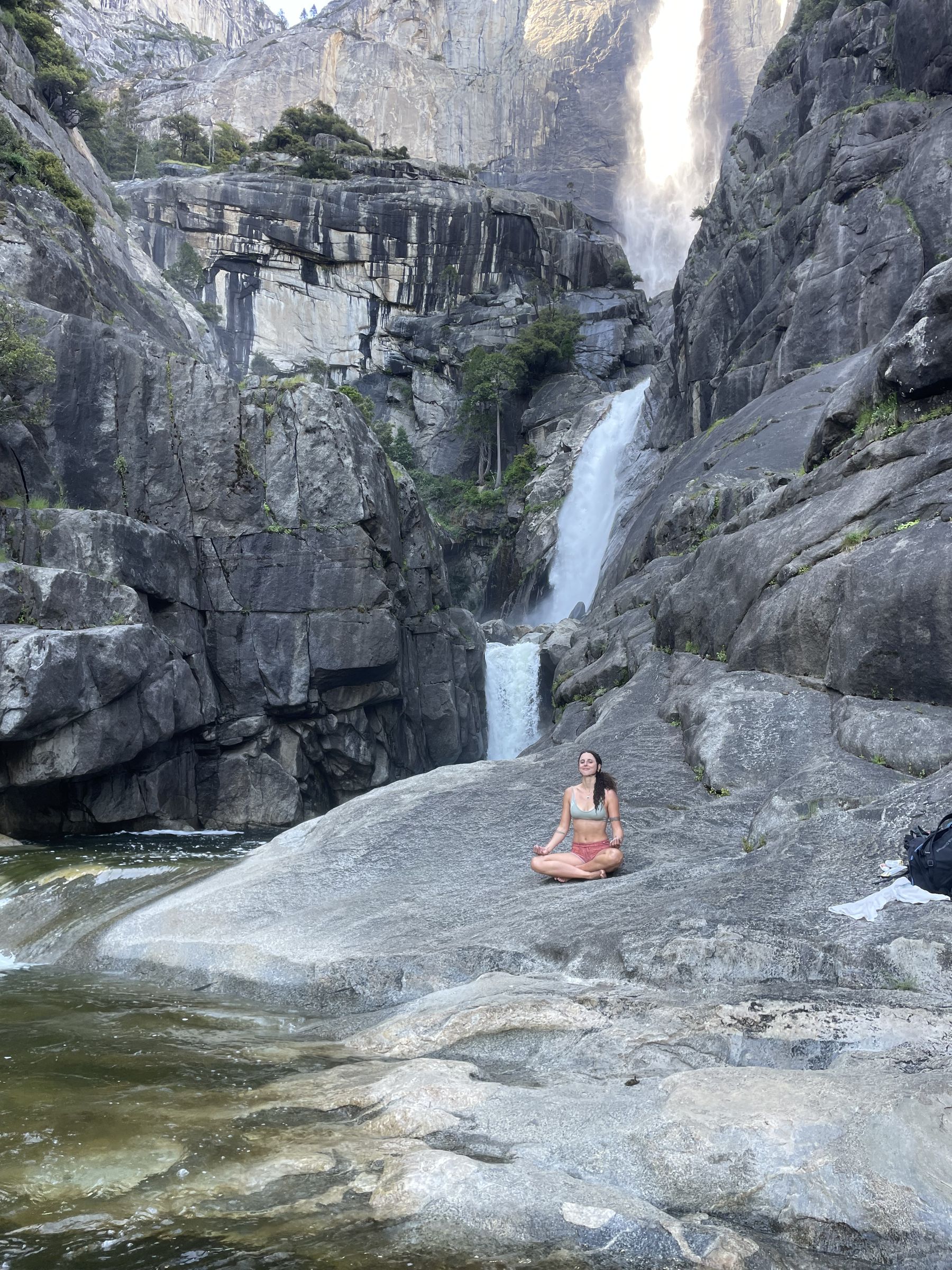 A woman meditating in lotus pose on a granite rock before a waterfall