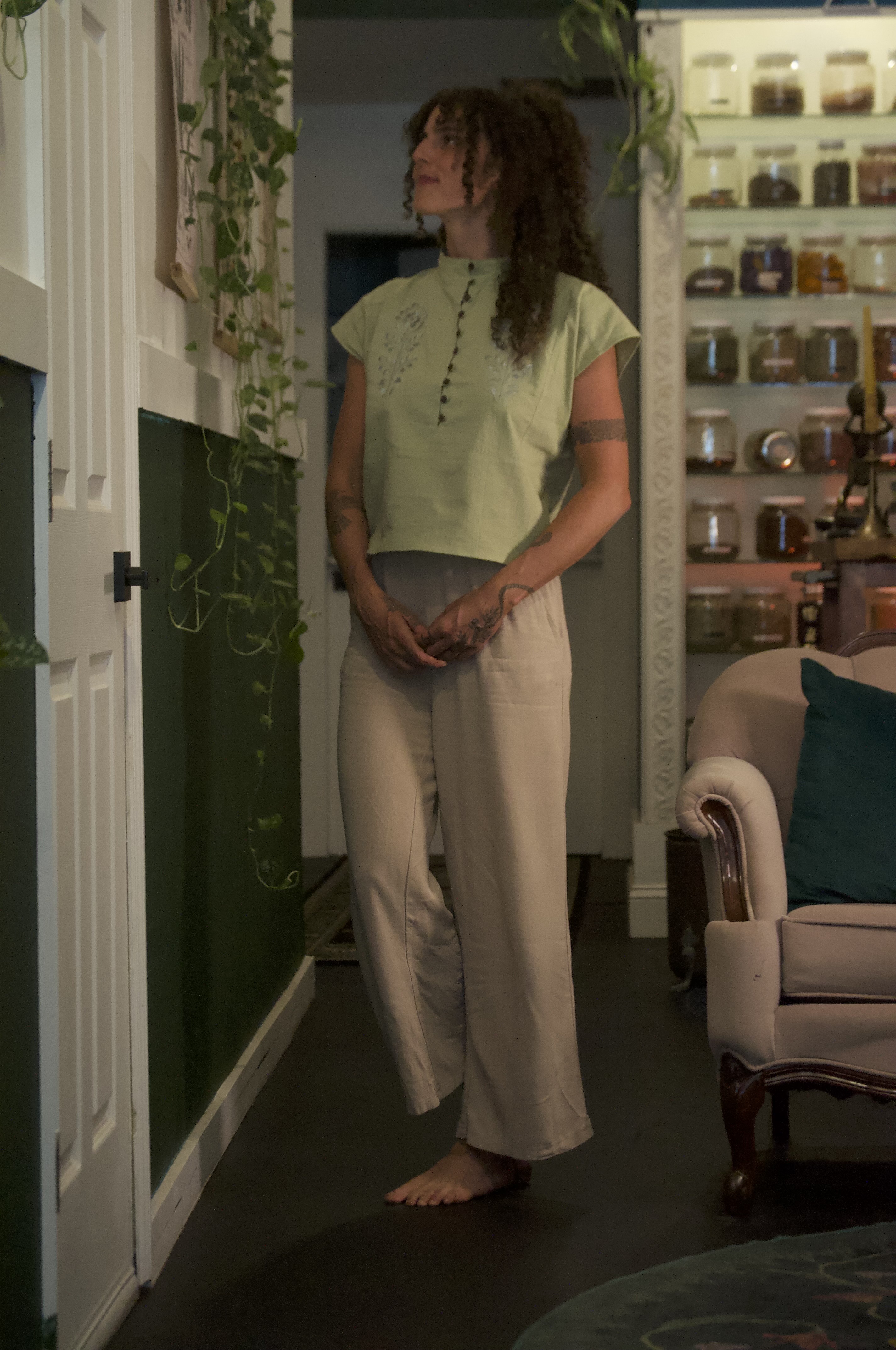 Alora Dawn standing in her apothecary surrounded by plants and herbal jars